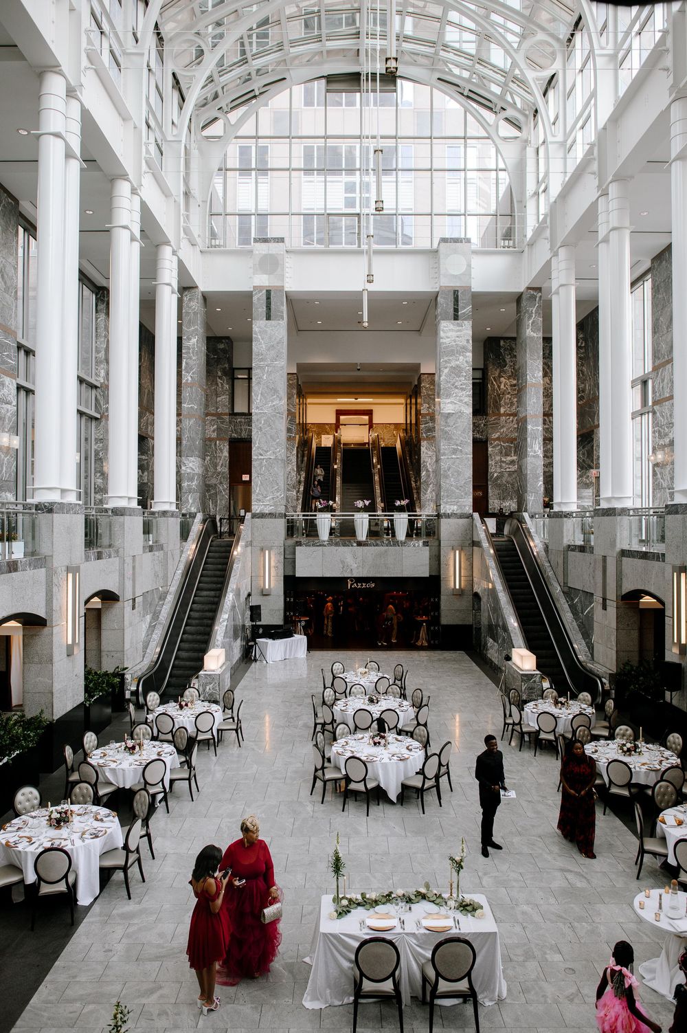 Elegant white dining room with marble columns, escalators, and round tables set for a formal event.