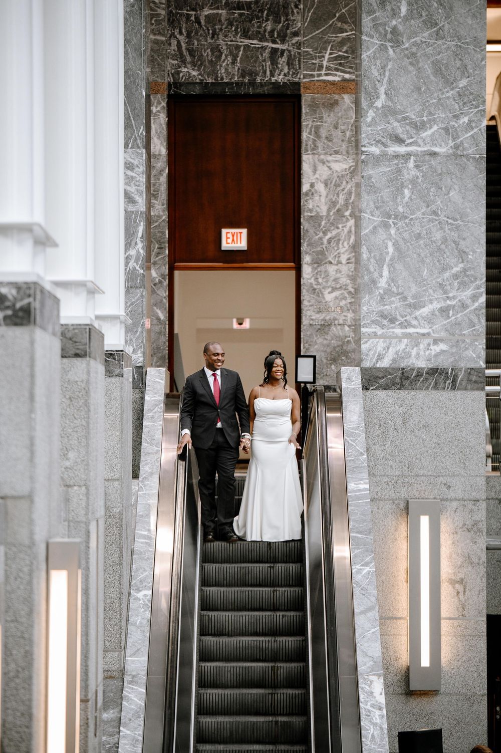 A series of photos showing a couple descending marble stairs in a grand building during their wedding ceremony.
