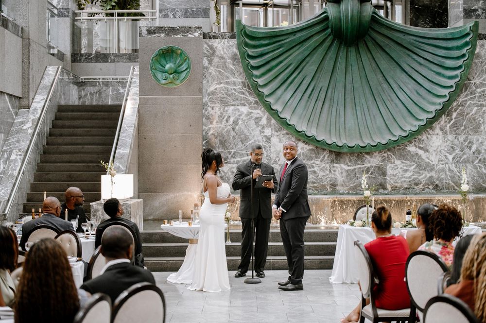 Wedding guests stand in formation on grand marble steps decorated with elegant green fan-shaped drapery.