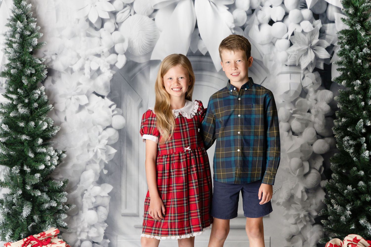 Girls sit together in a white and green holiday setting surrounded by winter decorations and presents.