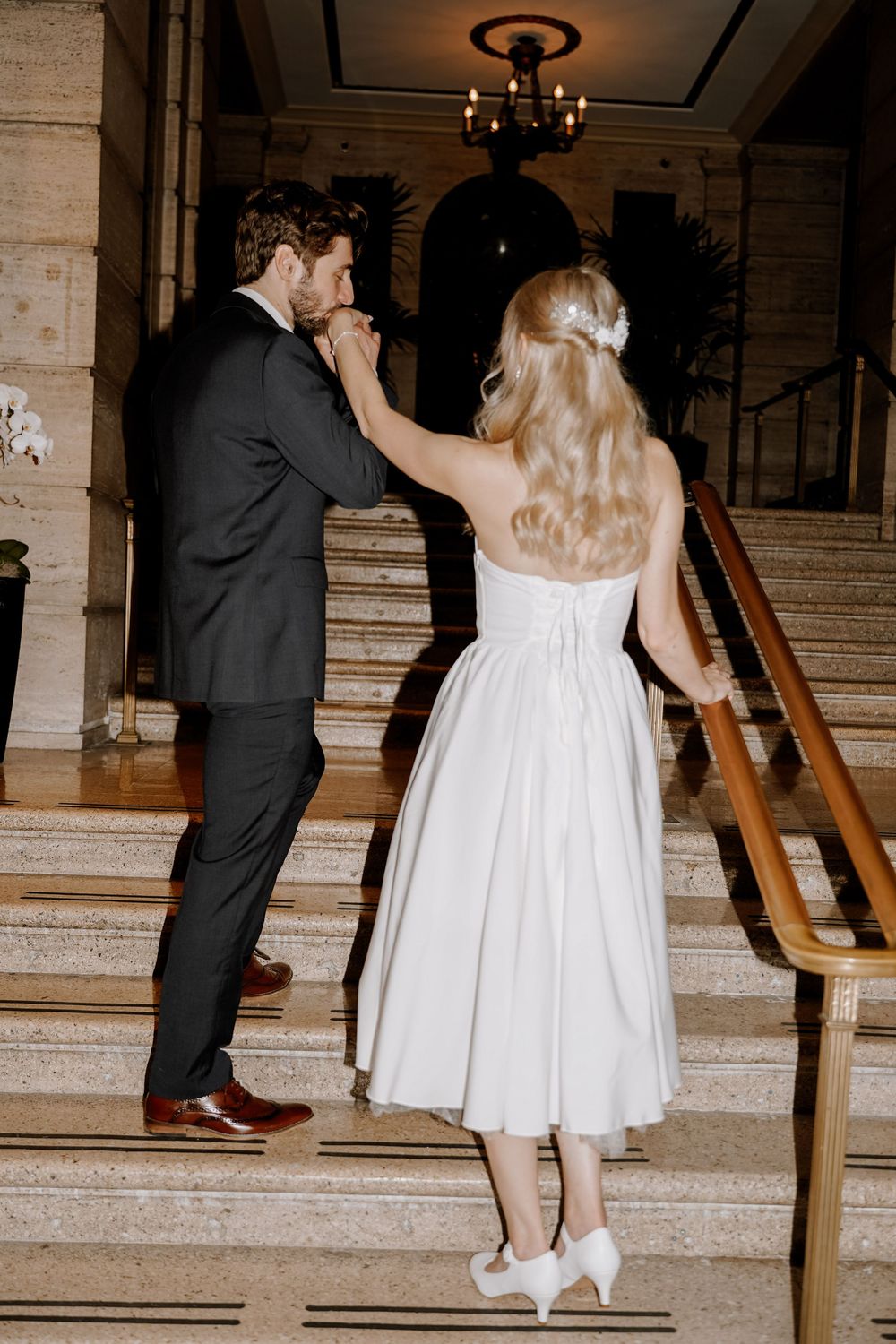 Couple ascending marble stairs together in wedding attire at an elegant venue.