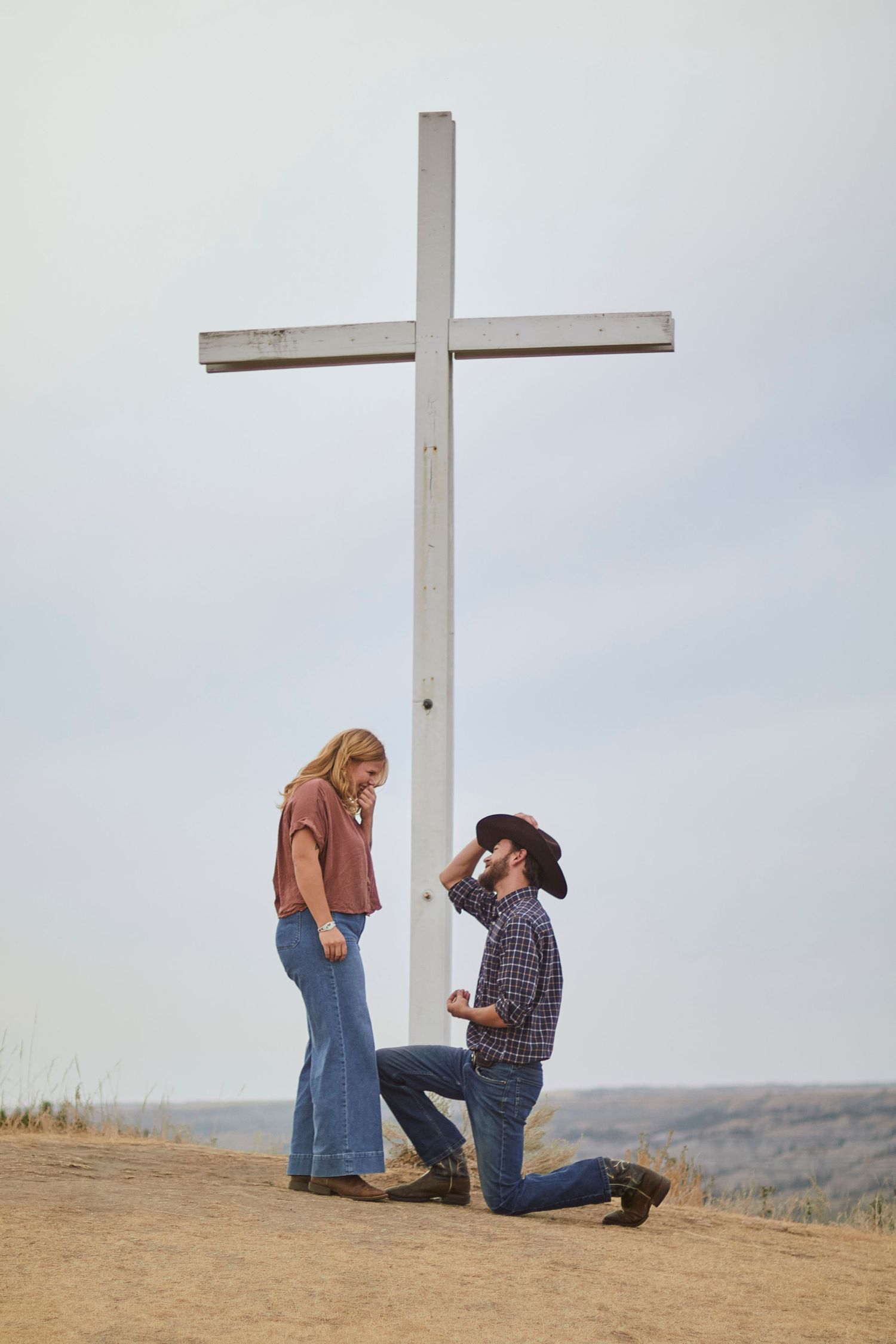 Couple engagement photoshoot with a cross in the background and the man on his knee proposing