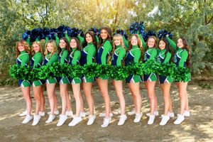 A group in matching green outfits and white shoes pose in a line against a sunlit outdoor backdrop.