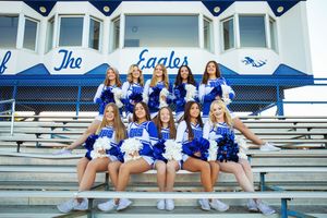 High school cheerleaders perform a synchronized split formation while posing on outdoor stadium bleachers.
