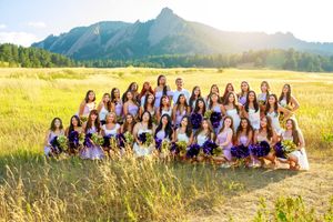 A group sits together in an open field with golden grass and mountain peaks at sunset in a scenic landscape.