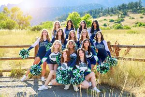 Cheerleaders in blue and white uniforms pose together outdoors against a scenic mountain landscape background.