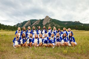 A sports team in blue and white uniforms sits in a row against a scenic mountain landscape background for team photos.