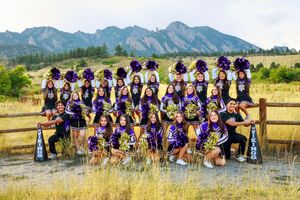 Large group in purple outfits sitting on wooden fence against mountain backdrop with Colorado Flatirons vista.