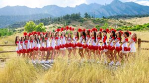 Beach cheerleading squad dressed in red and white performs a synchronized line formation at sunset on sandy shore.