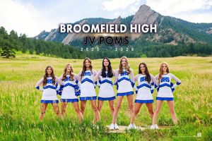A group of cheerleaders in blue and white uniforms pose in a grassy mountain meadow on a sunny summer day.