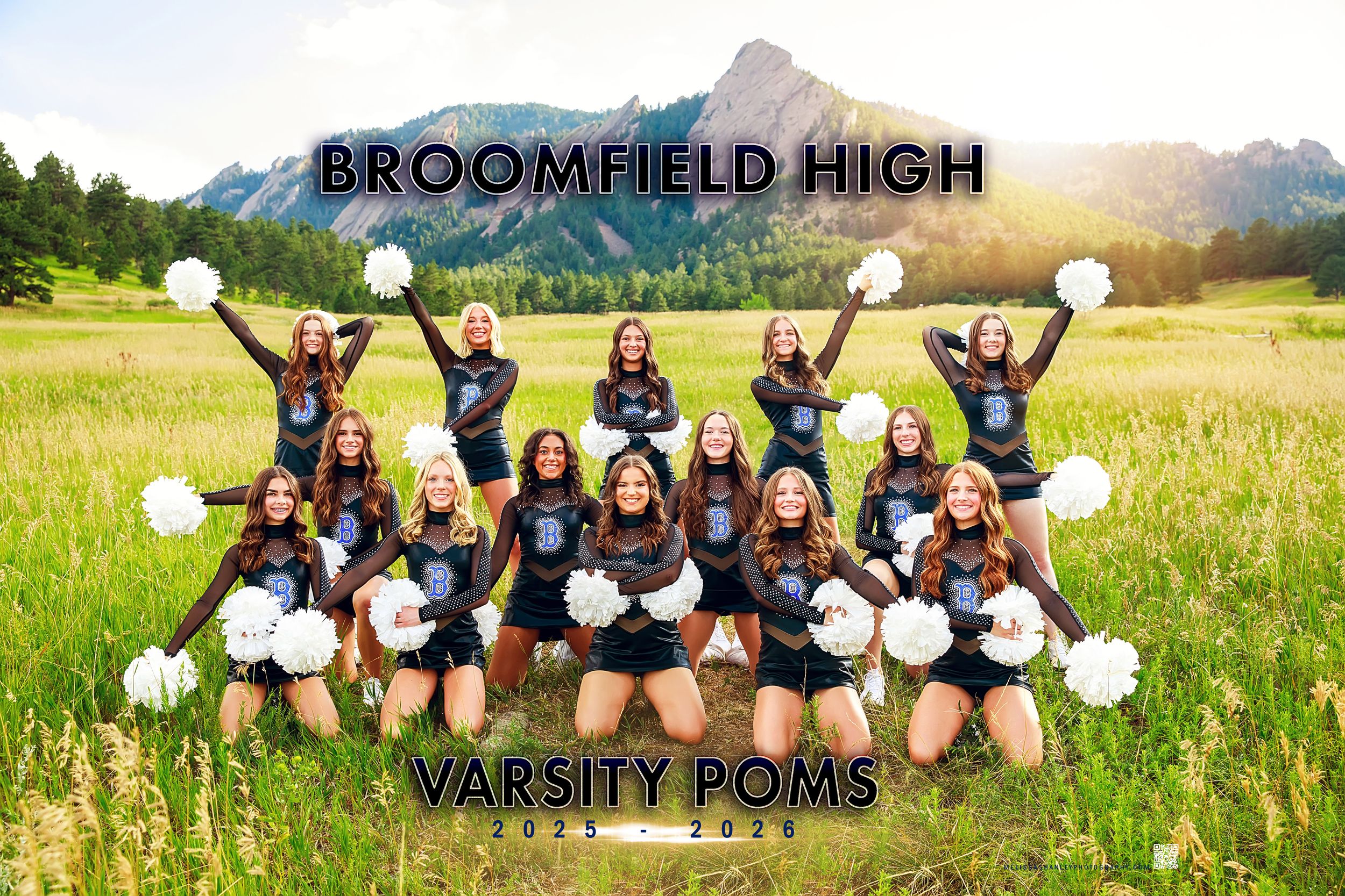 Cheerleading squad poses with pom poms in front of scenic mountain landscape on grassy field.