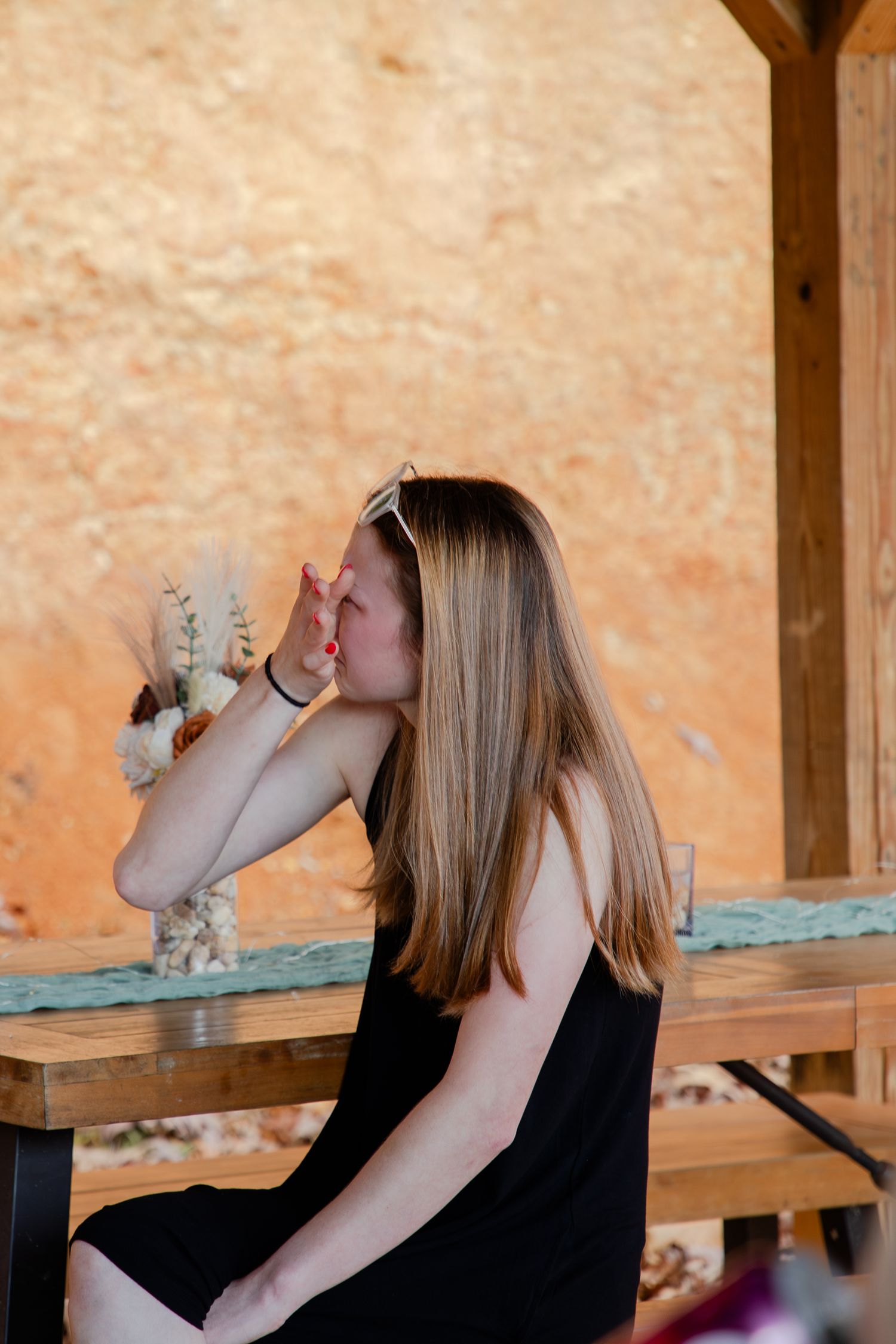 Person in black sleeveless top drinking from a glass bottle in a rustic wooden setting with warm lighting.