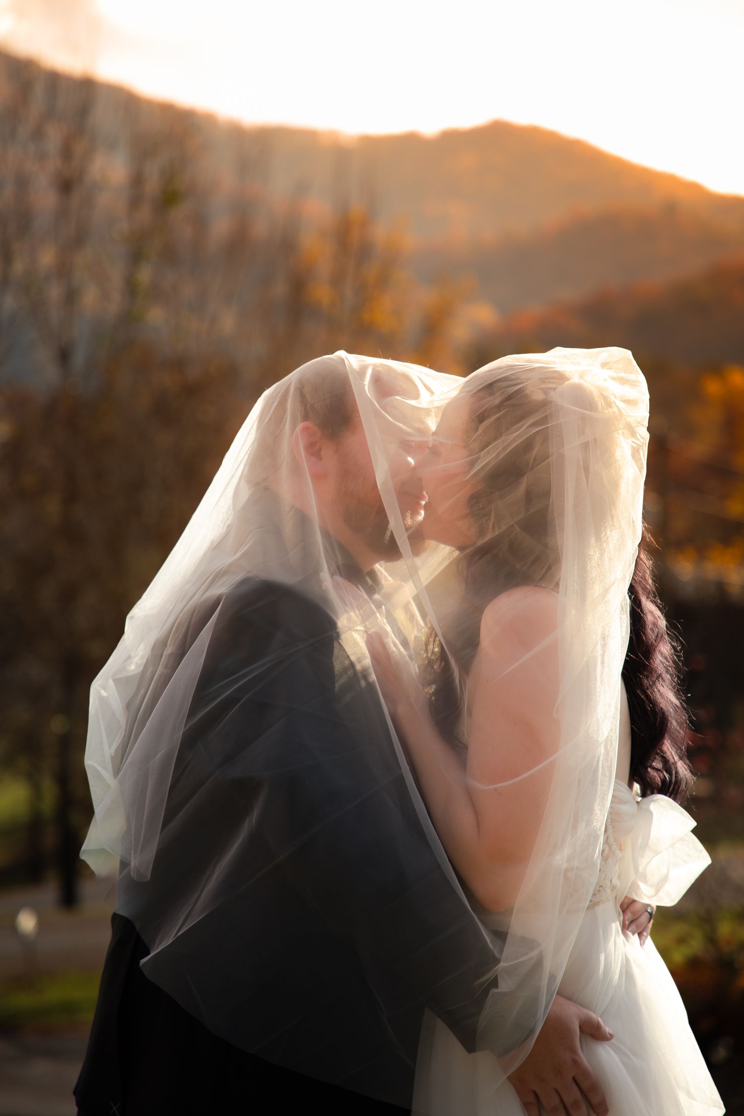 A romantic silhouette of a couple in wedding attire embracing at sunset with a flowing veil in the breeze.