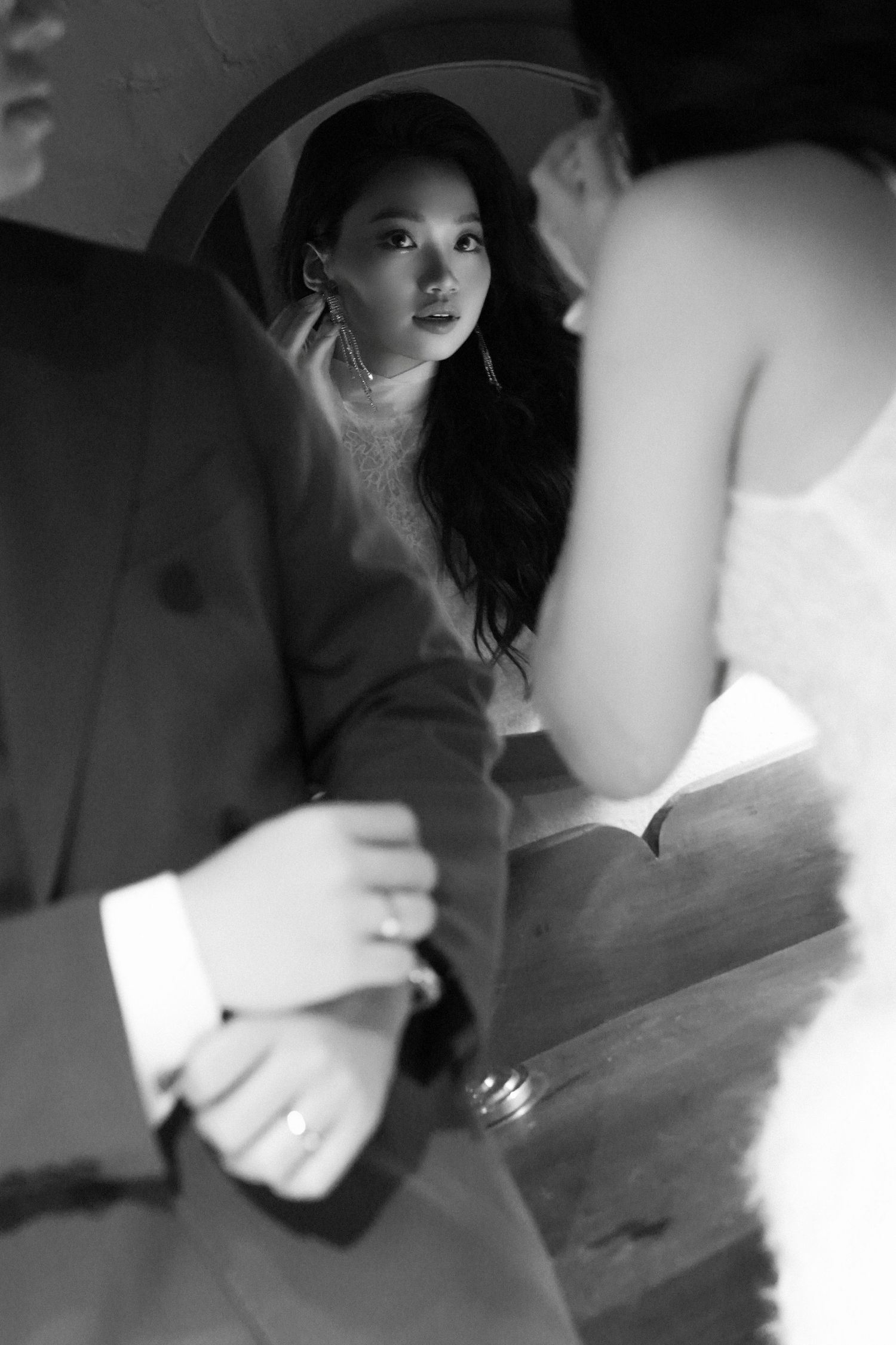 Black and white artistic shot of Asian bride reflected in mirror, groom's hand visible with wedding ring.