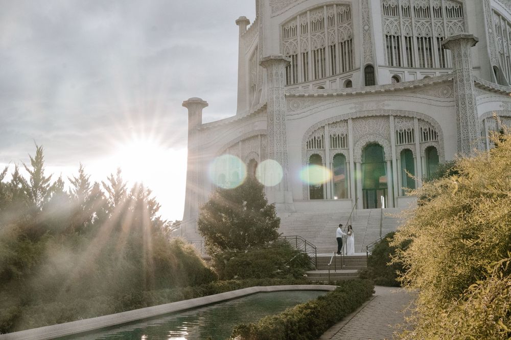 Dramatic sunburst through trees illuminates the white domed Baha'i House of Worship with landscaped garden in foreground.