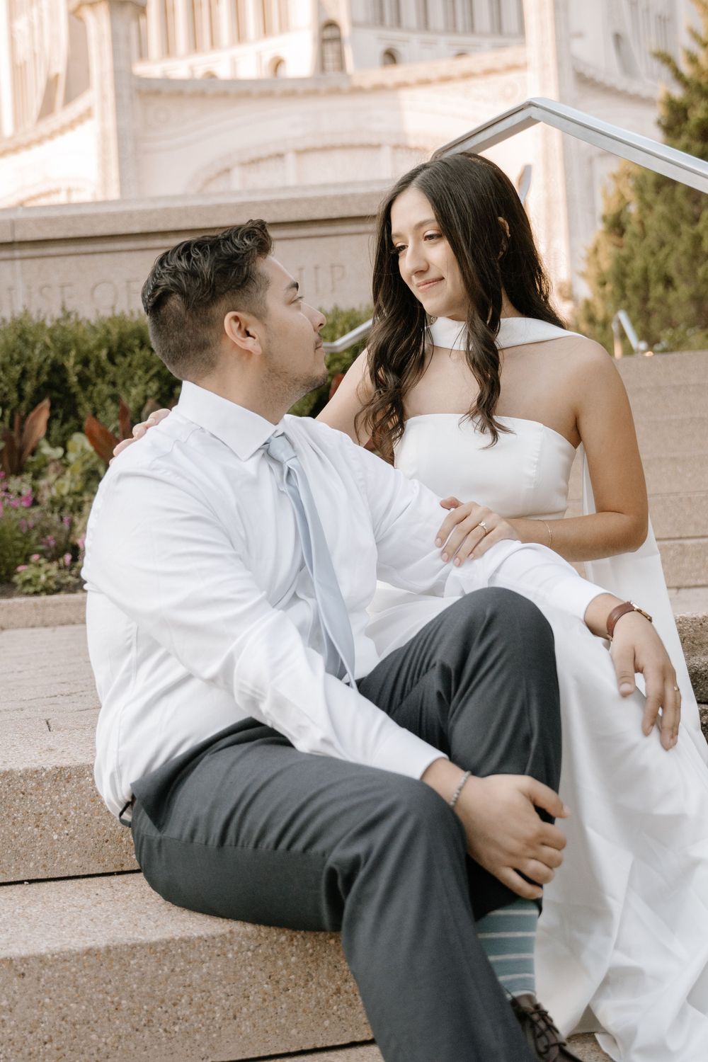 Couple in wedding attire playfully posing on steps of a grand white building.