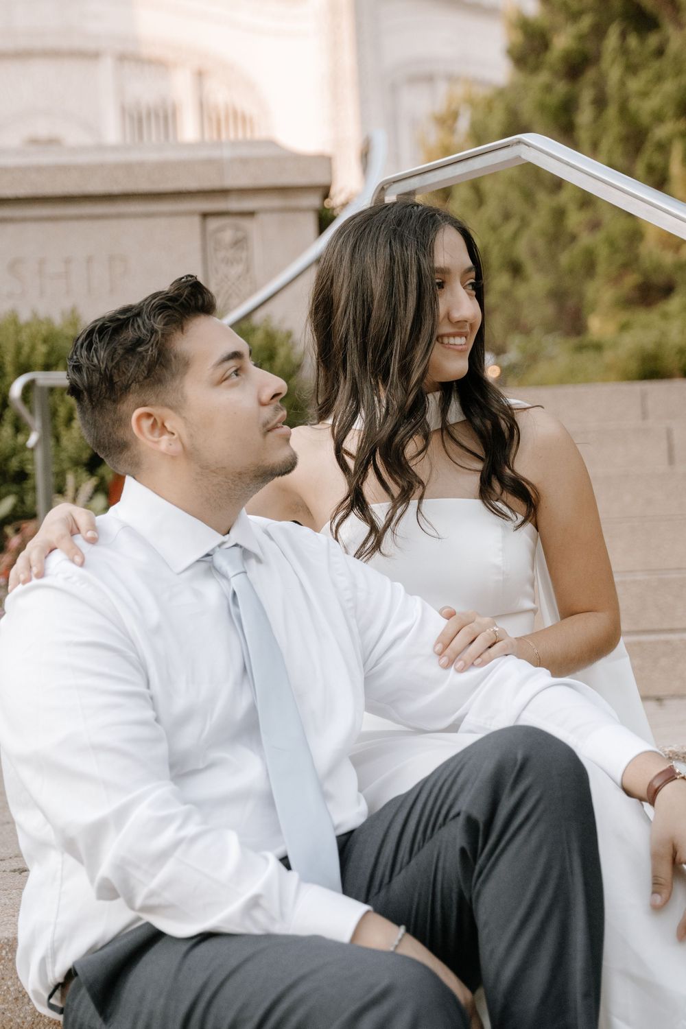A romantic couple sitting in relaxed poses on stone steps while dressed in formal black and white attire.