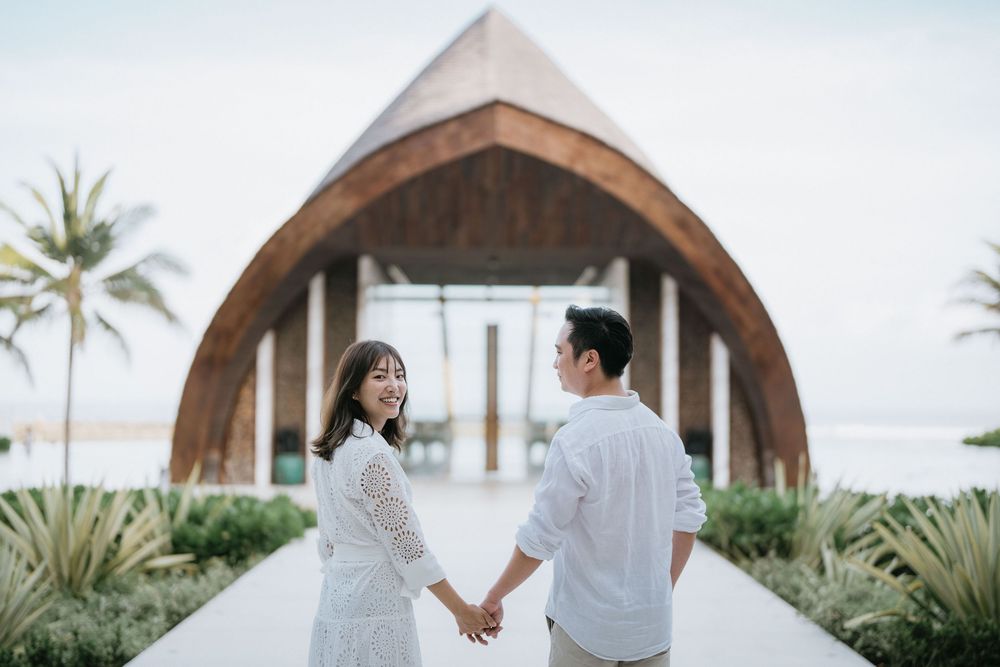 Couple holding hands in front of a modern wooden chapel with palm trees.