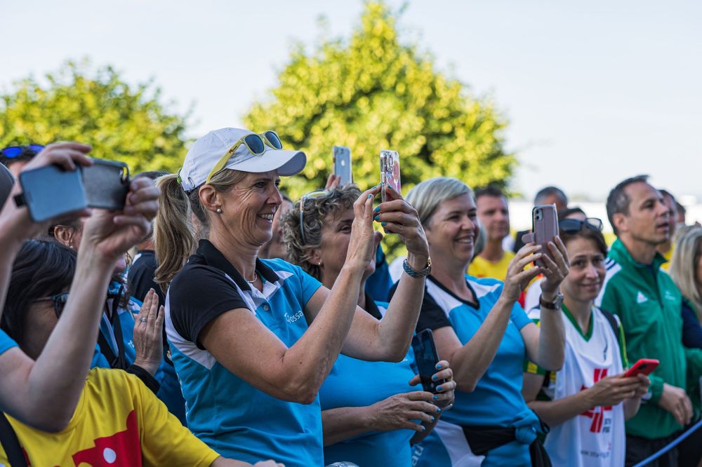 Crowd of spectators hold up phones to capture a moment at an outdoor sporting event on a sunny day.