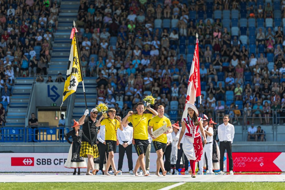 Soccer players from two teams line up on the field before a match at a crowded stadium during a sunny day.