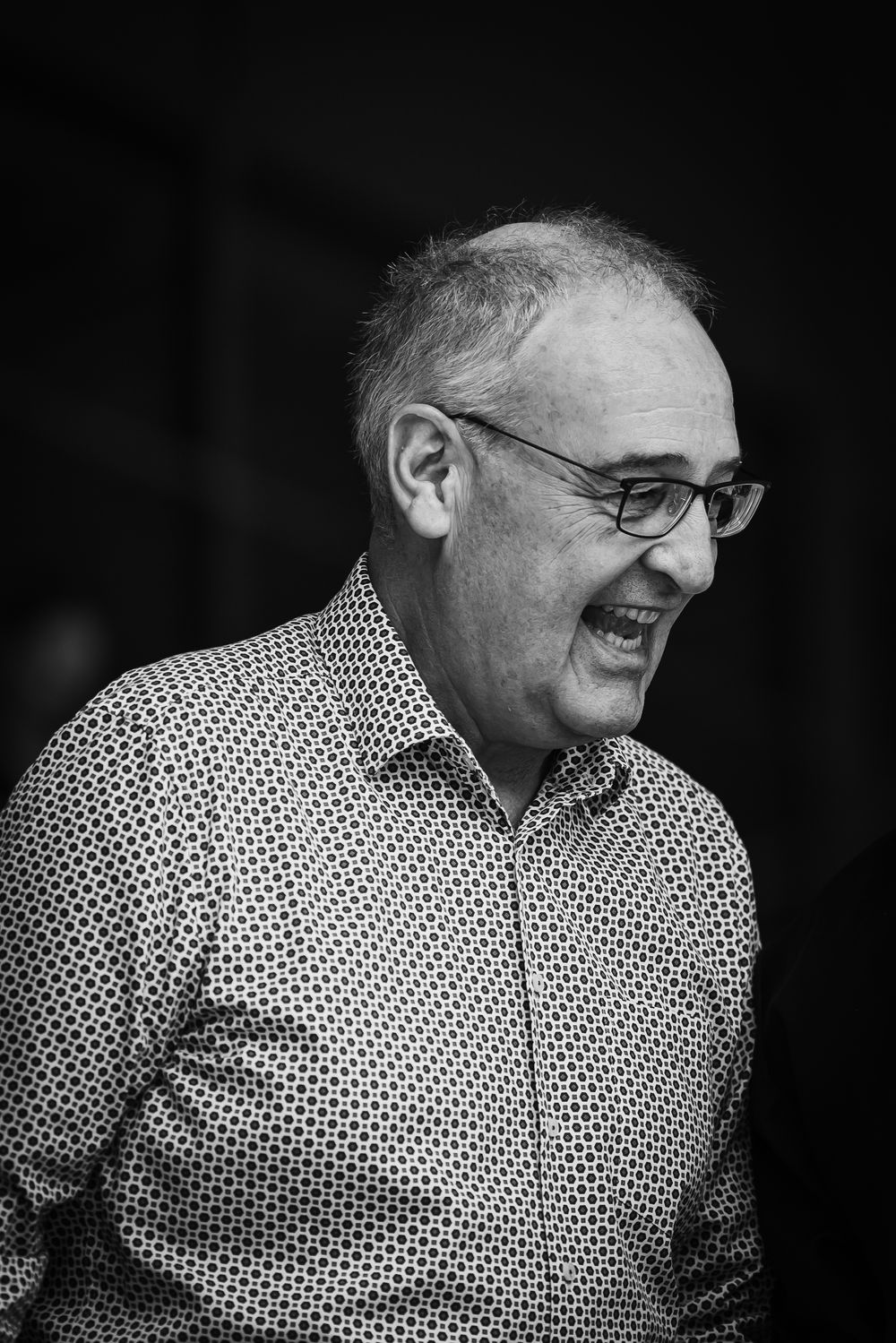 A person in a polka dot shirt laughs heartily while looking to the side in a black and white sequence of images.