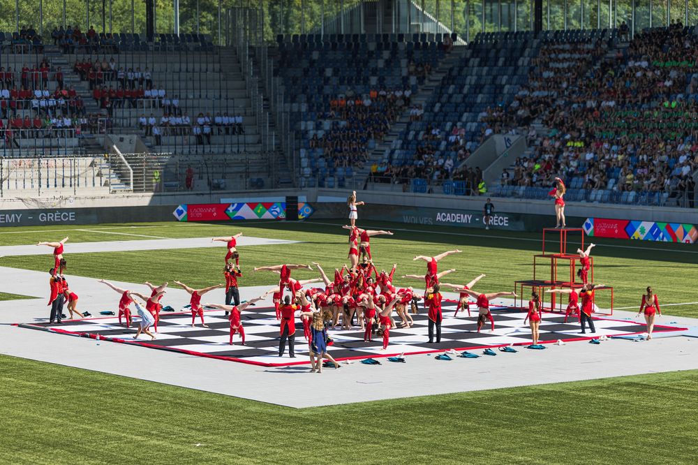 A cheerleading squad performs a dynamic routine on a white mat in a stadium with red uniforms and precise formations.