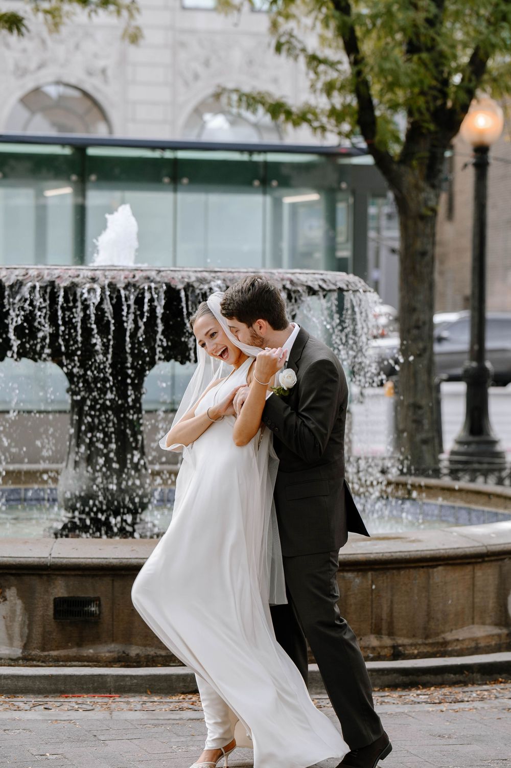 A romantic wedding couple dances and twirls near a fountain with string lights creating a magical atmosphere.