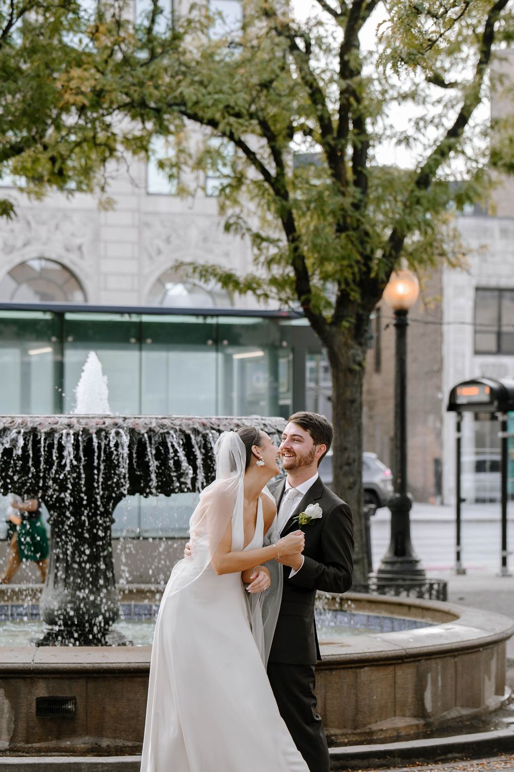 A romantic wedding couple shares intimate moments by a fountain in an urban setting during their special day.