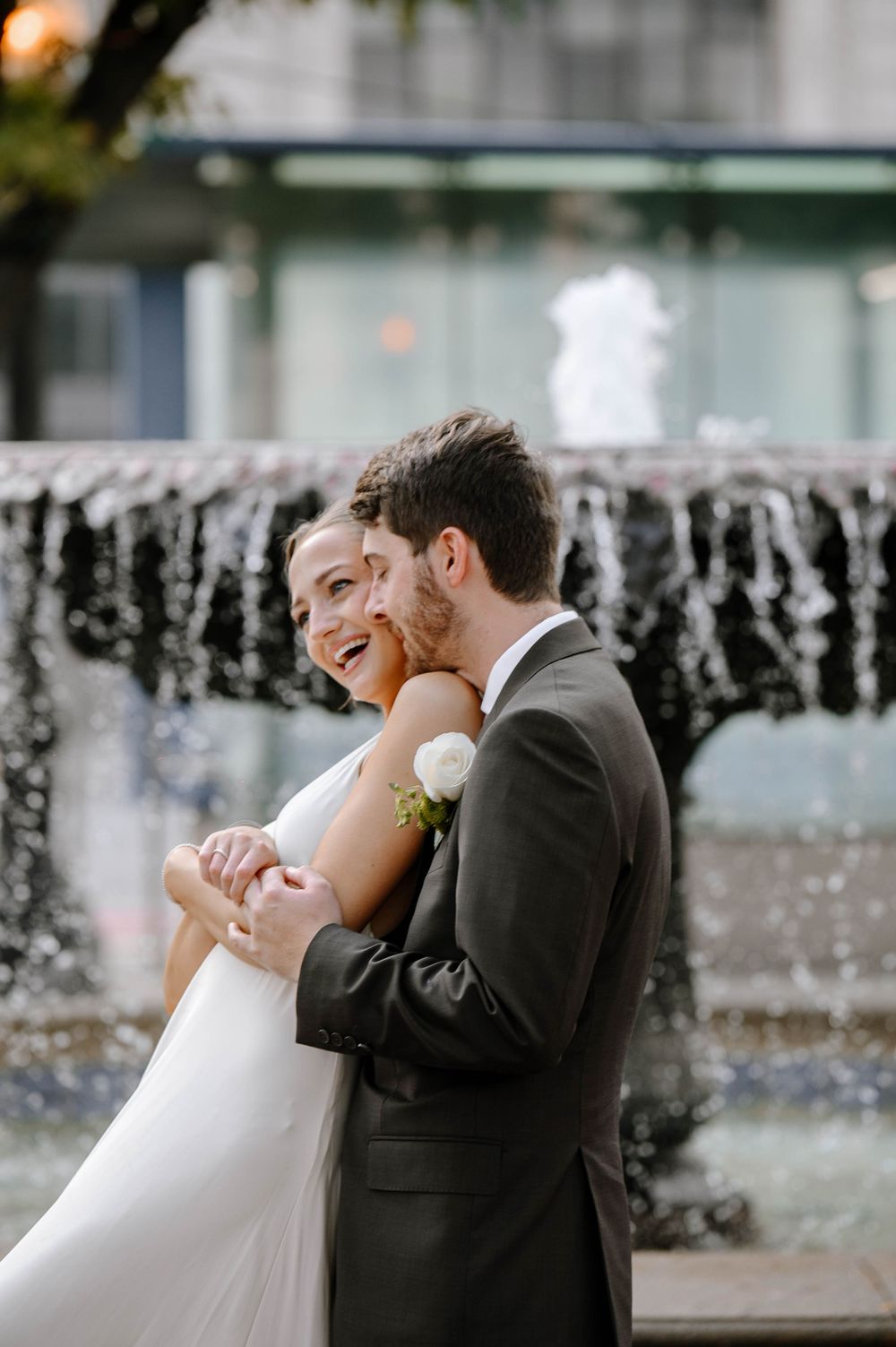 Romantic couple embraces near a cascading fountain in an elegant outdoor setting.