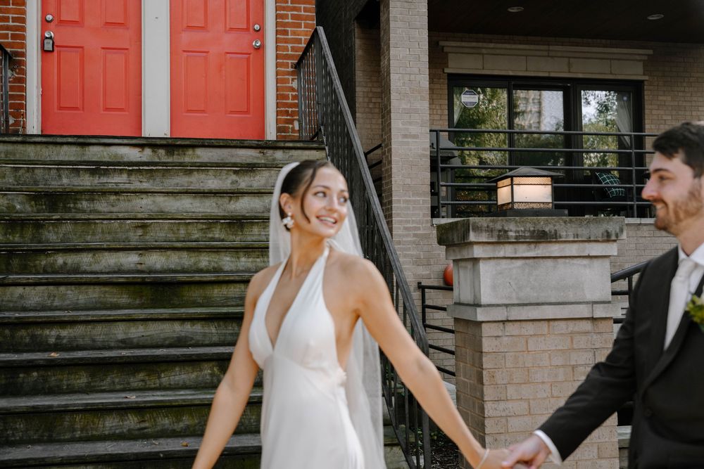 A couple in formal wedding attire share a romantic moment on a stone staircase with red doors in the background.