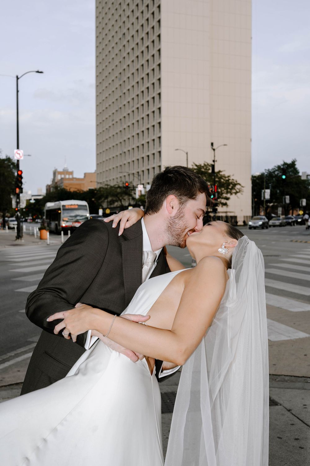 Romantic dip kiss between newlyweds in front of modern urban building on their wedding day.