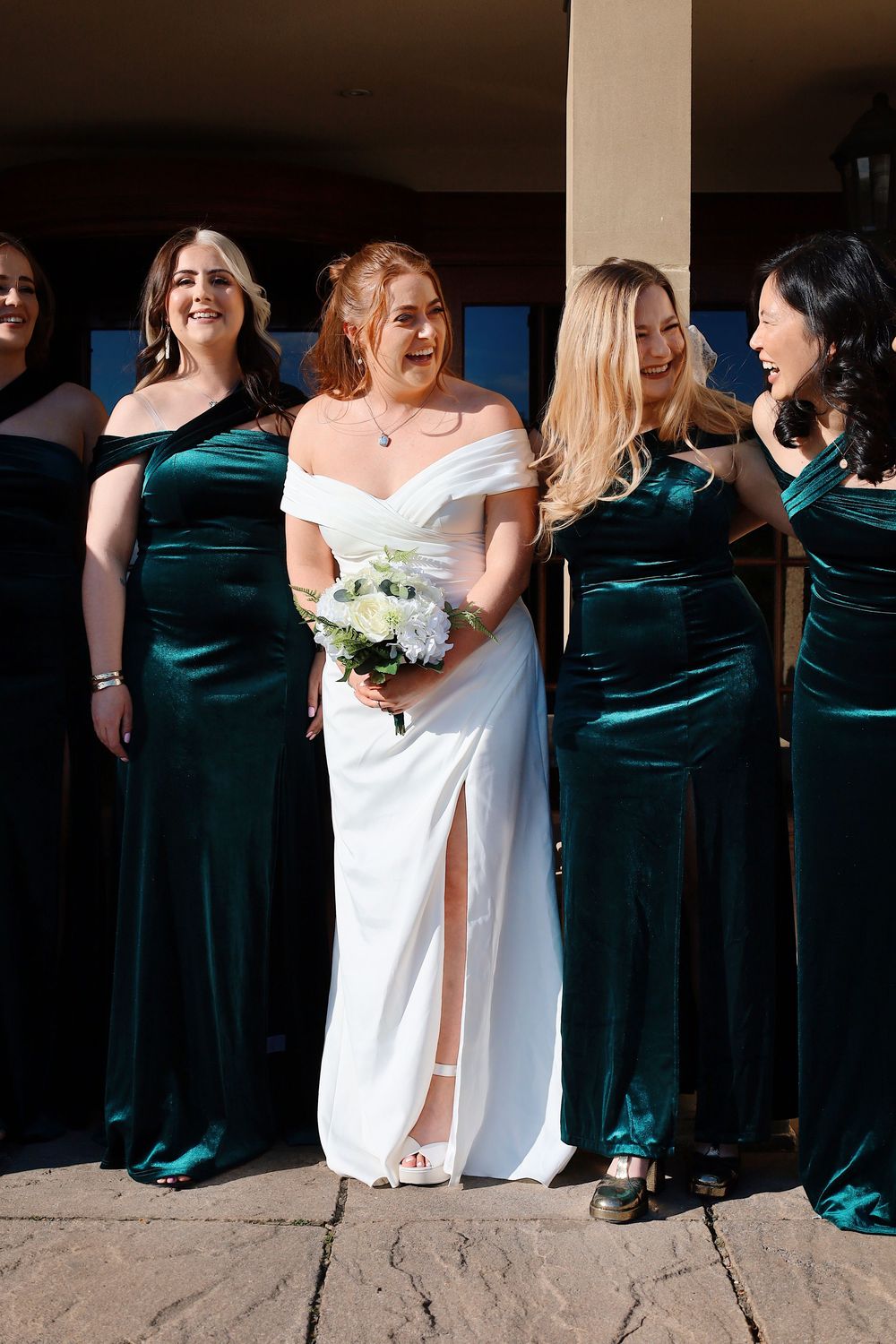 Bridal party in white and teal dresses posing together outdoors.
