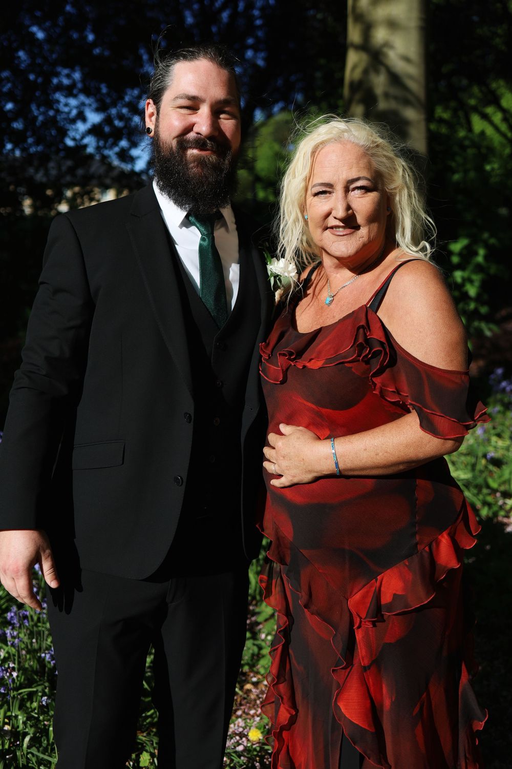 A formal portrait of two people in evening attire standing together in a garden setting.