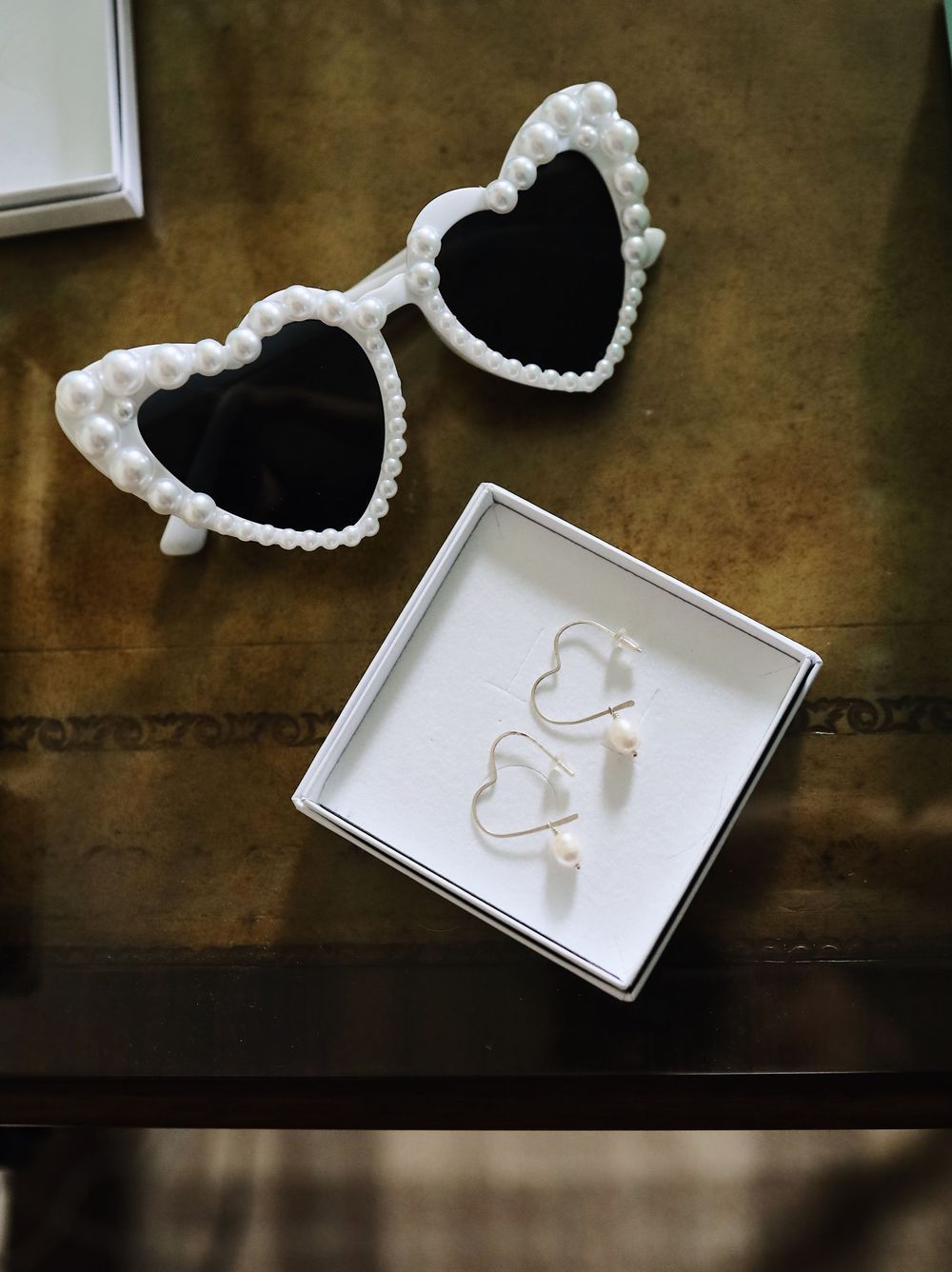 Heart-shaped white lace sunglasses and matching earrings displayed on a wooden surface.