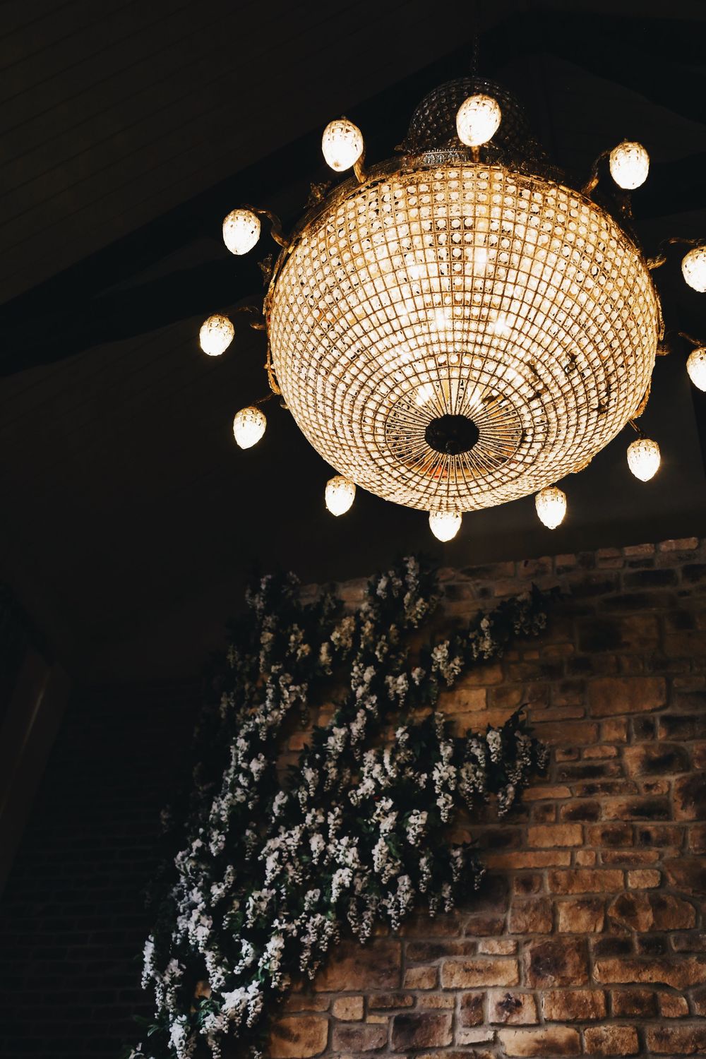 An elegant crystal chandelier illuminates a brick wall with cascading floral decorations.