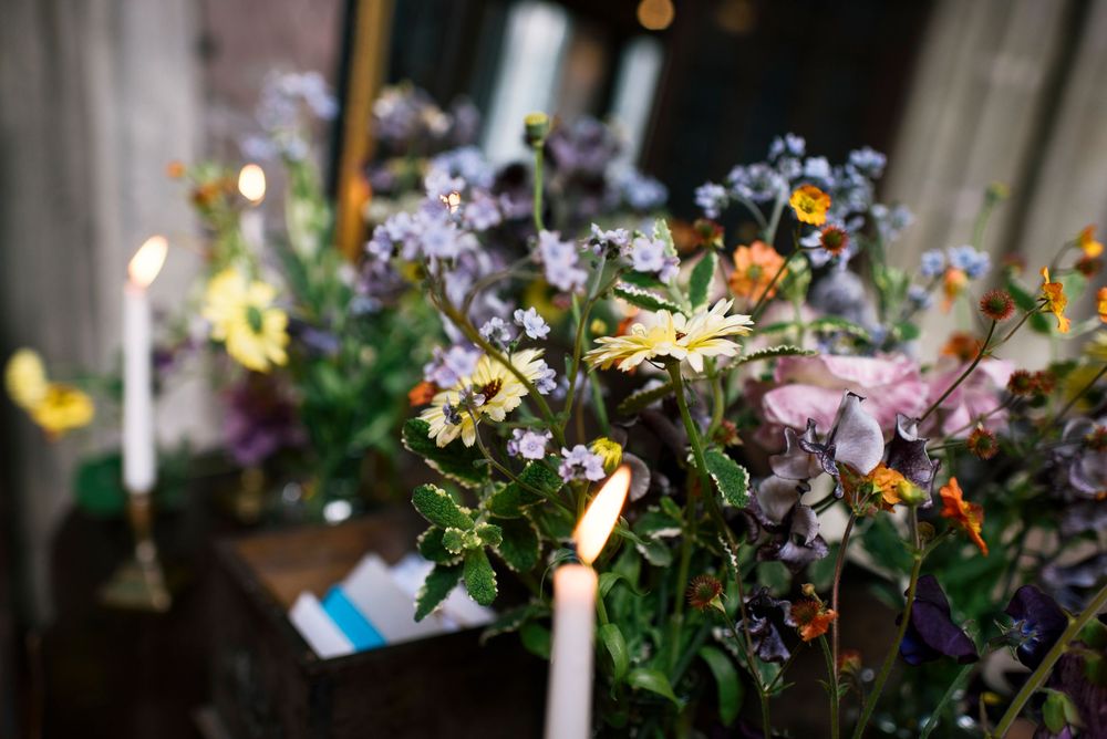 Delicate wildflower and candle arrangement on wooden surface in dim lighting.