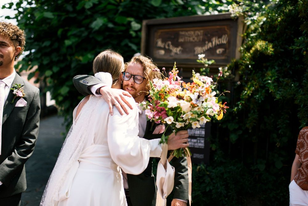 Wedding party celebrates outdoors in formal attire surrounded by greenery and natural light.