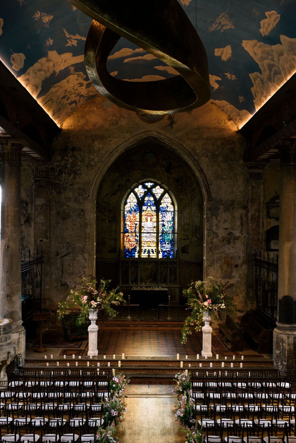 Gothic church interior with rows of chairs and stained glass windows illuminating the stone walls and vaulted ceiling.