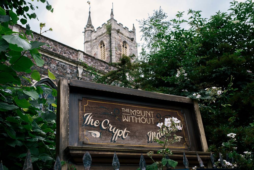 A medieval church tower and grounds surrounded by lush green trees in a historic English countryside setting.