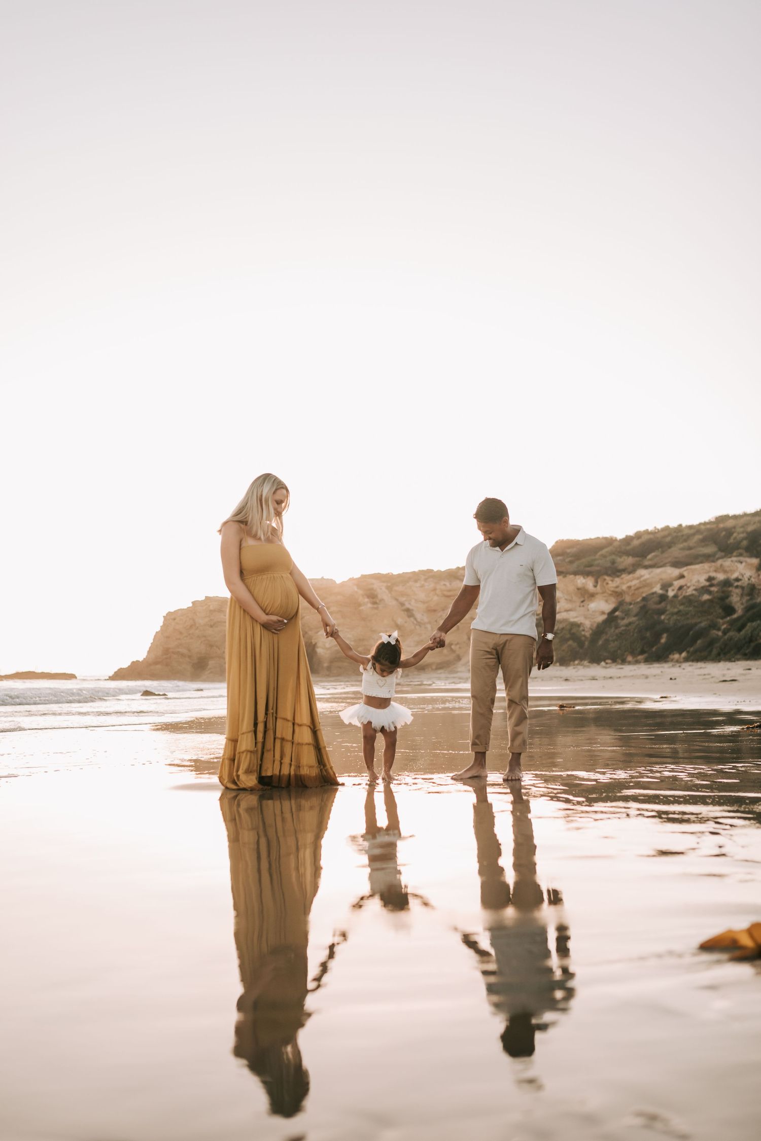 Family bonding together at the beach during sunset with reflections in wet sand and coastal cliffs in background.