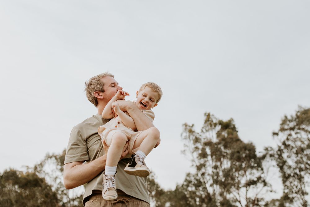 A dad cuddles his son tight and plays boisterously with him at golden hour during a photoshoot with Lauren Lunn Photography in Adelaide.