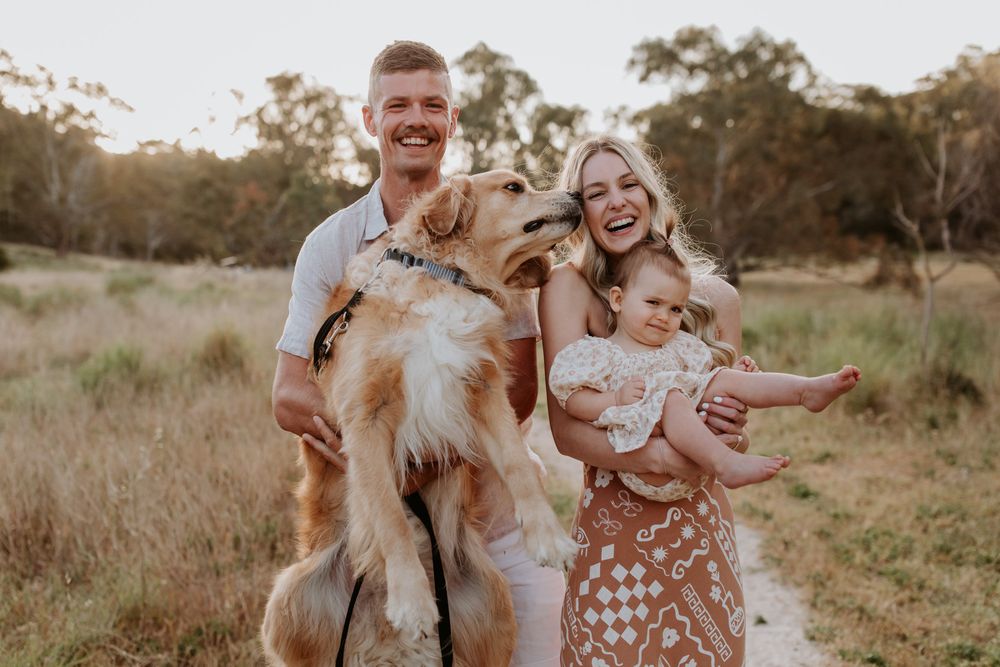 Parents and their baby girl hug their dog in sunlit field during Adelaide family session with Lauren Lunn Photography at Sunset.