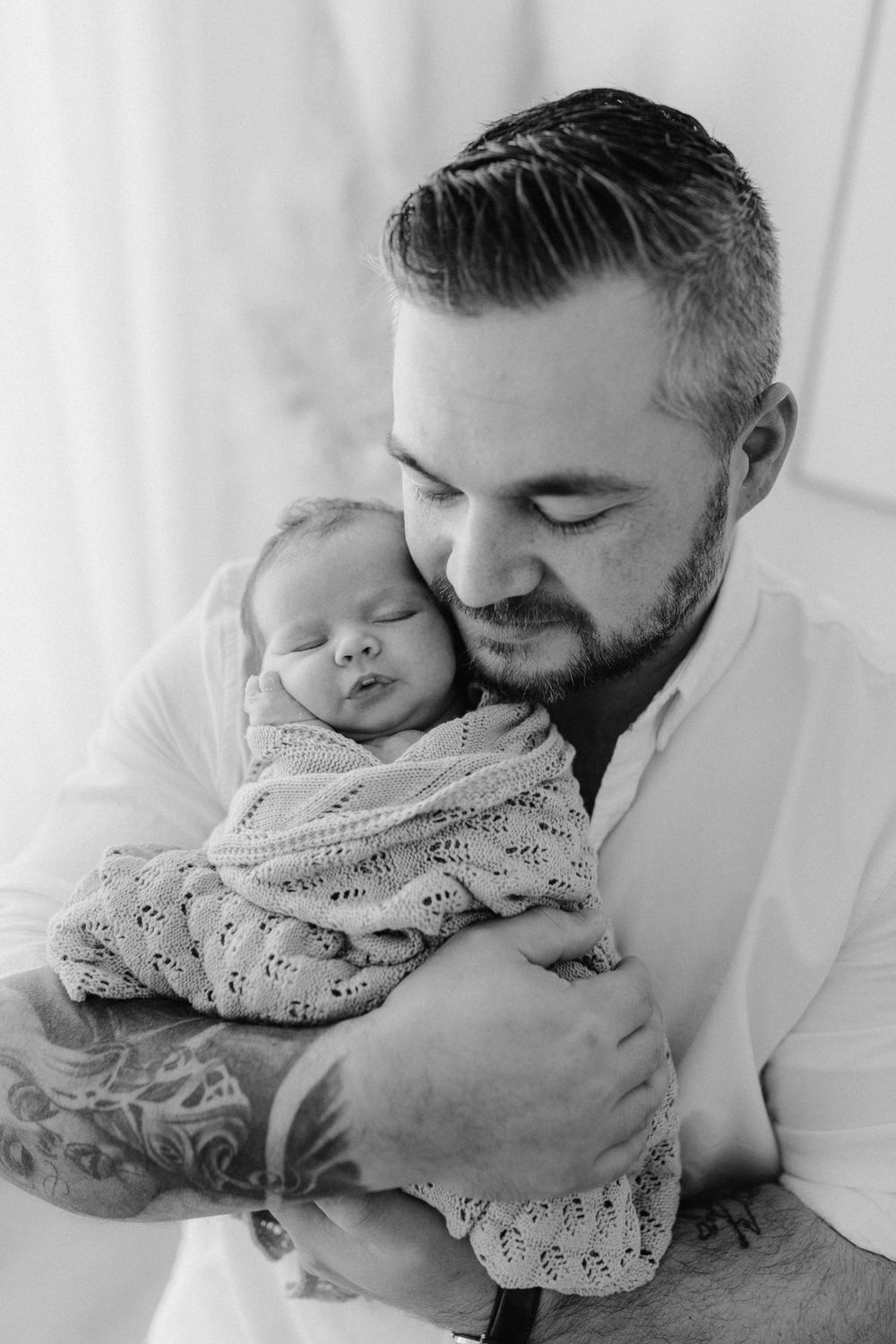 Lauren Lunn Photography captures a Black and White image of dad holding his newborn baby in Tea Tree Gully studio, wrapped in neutral tones.
