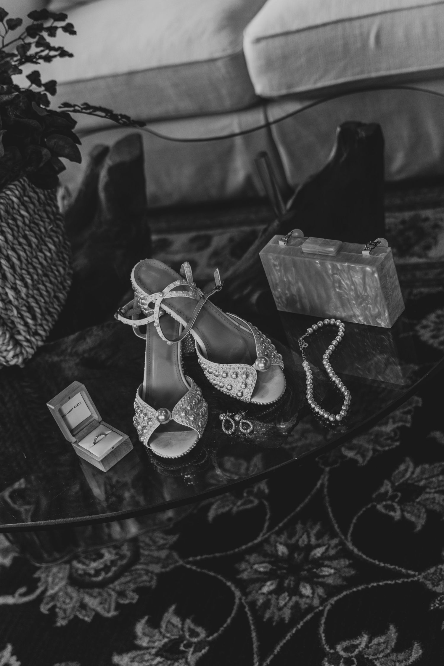 Elegant bridal shoes and delicate silver jewelry displayed on dark floral lace fabric for wedding preparation.