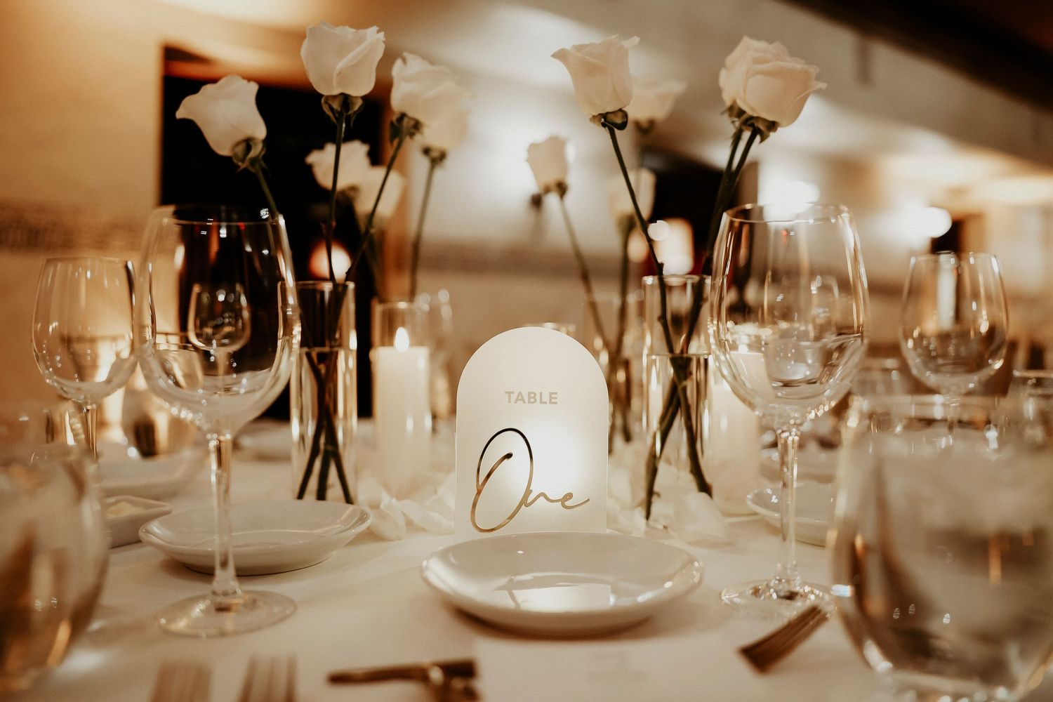 Elegant table setting at an event with wine glasses, candles and soft lighting casting a warm amber glow.