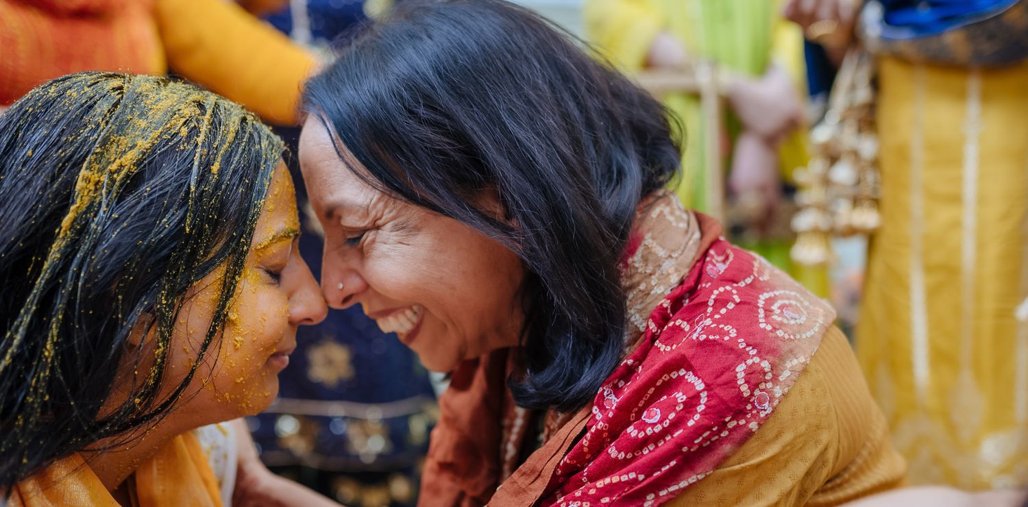 Bride and groom covered in turmeric during an Indo-Norwegian wedding and Family applying Haldi to the bride during a joyful wedding ritual