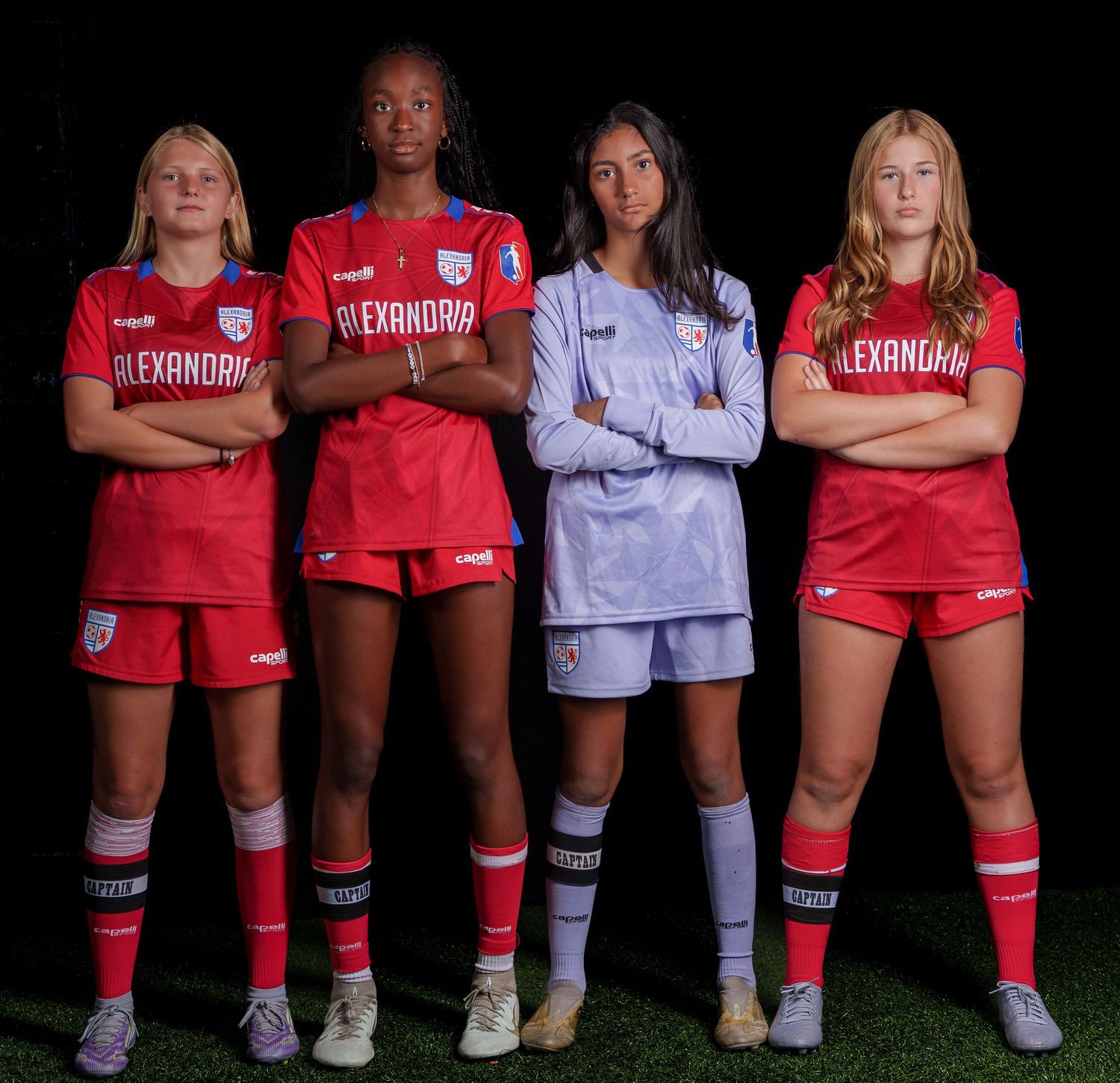 Group of soccer players wearing red and white uniforms pose for a team photo on a dark field with colored socks.
