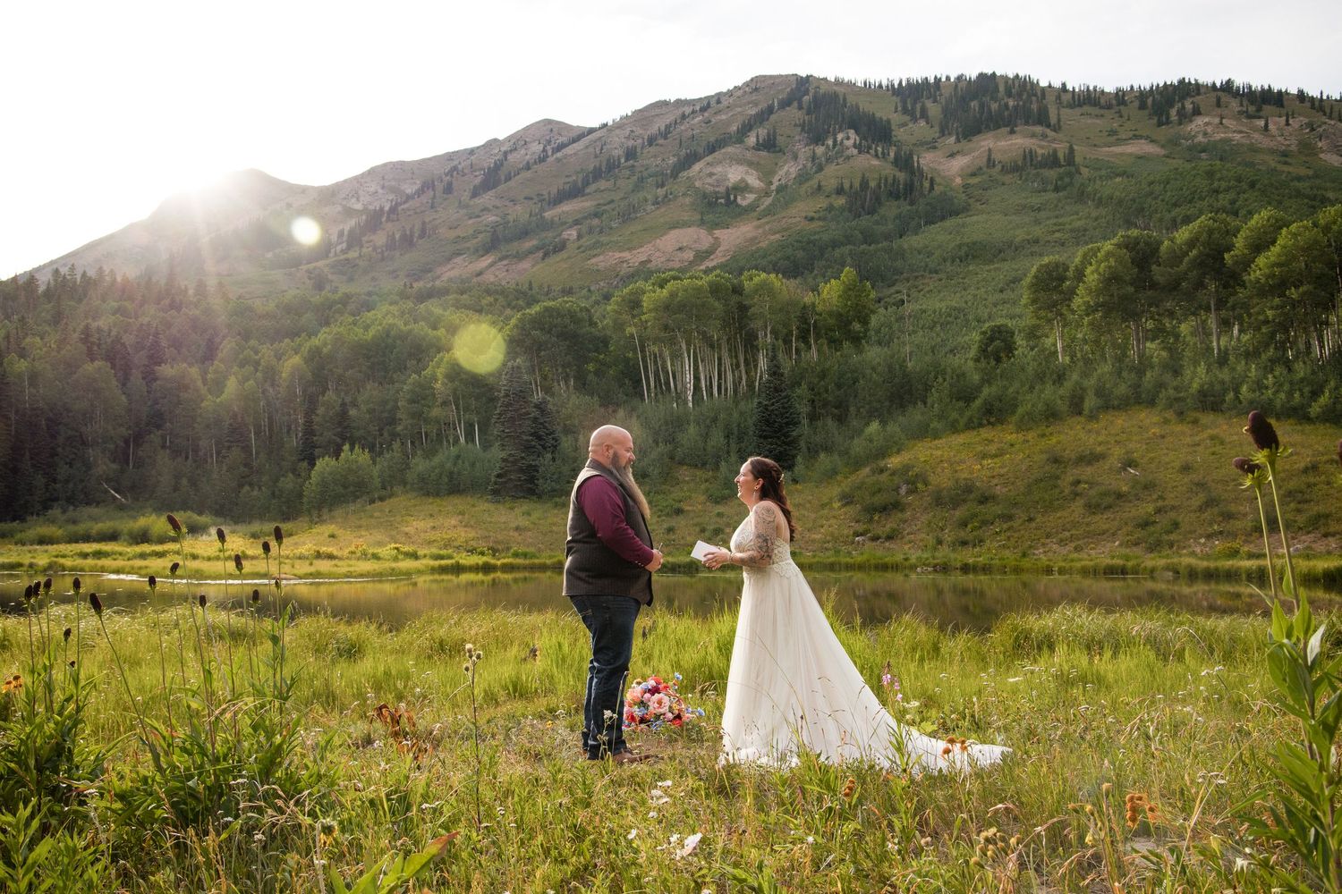 Wedding couple stands in a scenic mountain landscape with lush green hills and dramatic sunlight in Scotland.