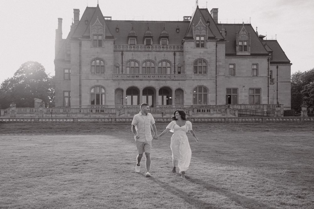 Couple strolling together on sprawling lawn in front of grand mansion at sunset.