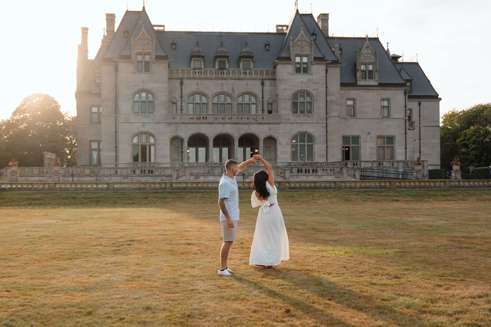 Two figures walking hand in hand across elegant estate grounds with stately mansion in background.